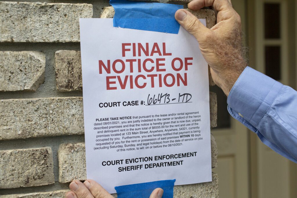 A person tapes a "Final Notice of Eviction" with a court case number to a brick wall near a door, highlighting concerns about baseless evictions, harassment, and retaliation from the court eviction enforcement sheriff department.
