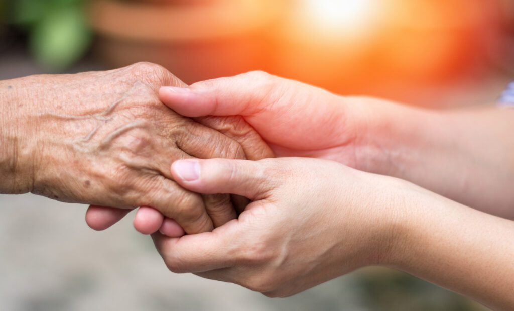 Close-up of a younger person gently holding an elderly person's hand, symbolizing care, support, and compassion—highlighting the importance of preventing Elder Abuse in Trusts and Probate—set against a warm, blurred background.