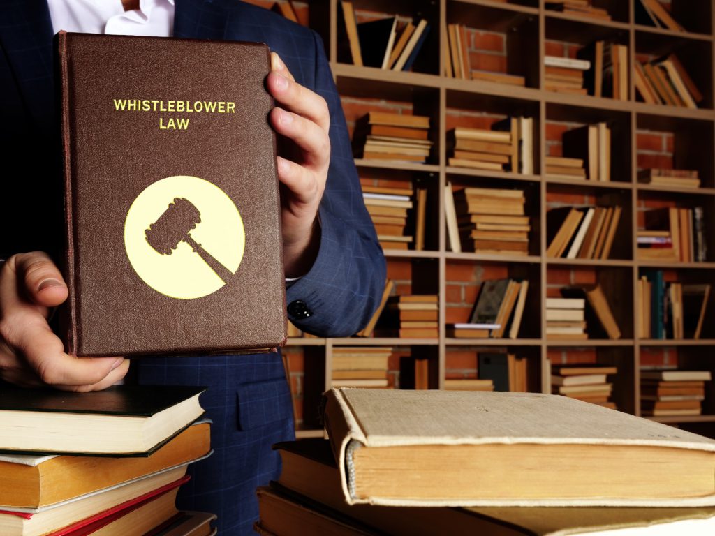 An attorney holding a book titled Whistleblower Law, representing California Labor Code section 1102.5 protection against workplace retaliation.