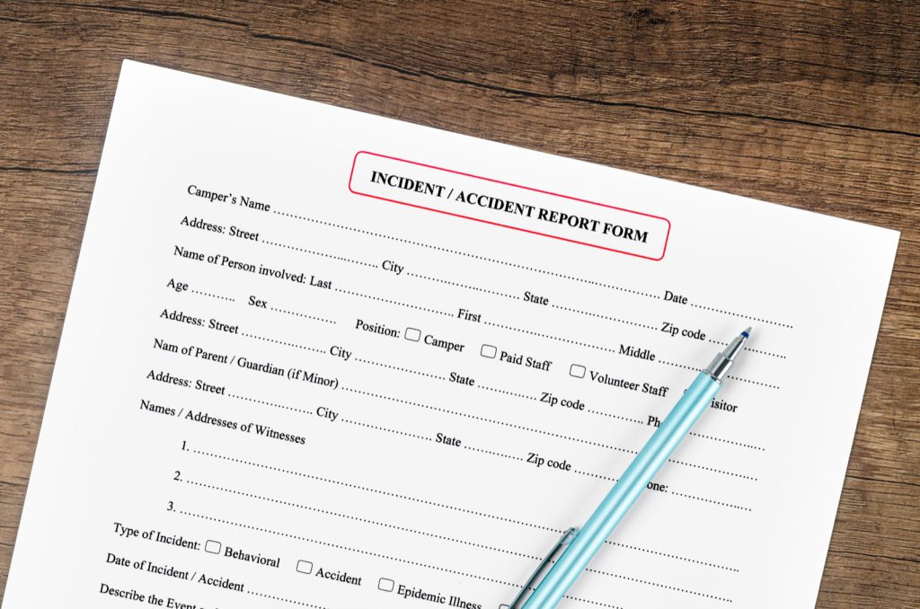 A blank accident report form and pen on a wooden desk, the incident report a business asks you to complete after a slip or trip and fall.