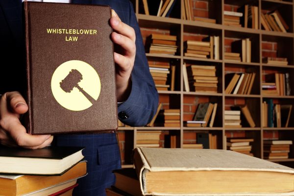 An attorney holding a book titled Whistleblower Law, representing California Labor Code section 1102.5 protection against workplace retaliation.