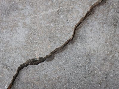 A deep settling crack and raised edge in a concrete sidewalk, the kind of dangerous condition that supports a California premises liability claim.
