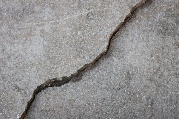 A deep settling crack and raised edge in a concrete sidewalk, the kind of dangerous condition that supports a California premises liability claim.