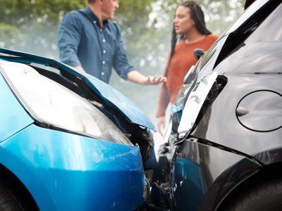 Two cars, one blue and one black, are shown after a head-on car accident. In the background, a man and woman discuss What to Do After a Car Accident. Both vehicles have significant front-end damage, highlighting the importance of protecting your rights after a crash.