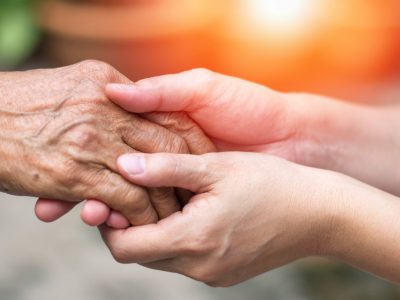 Close-up of a younger person gently holding an elderly person's hand, symbolizing care, support, and compassion—highlighting the importance of preventing Elder Abuse in Trusts and Probate—set against a warm, blurred background.