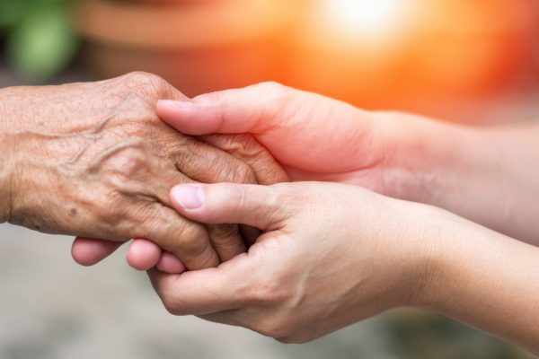 Close-up of a younger person gently holding an elderly person's hand, symbolizing care, support, and compassion—highlighting the importance of preventing Elder Abuse in Trusts and Probate—set against a warm, blurred background.