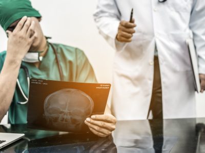 Medical Failure Concept - Surgical doctor covering his face with hand (face palm) expressing disappointment while holding xray film on office desk.