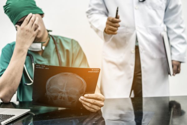 Medical Failure Concept - Surgical doctor covering his face with hand (face palm) expressing disappointment while holding xray film on office desk.