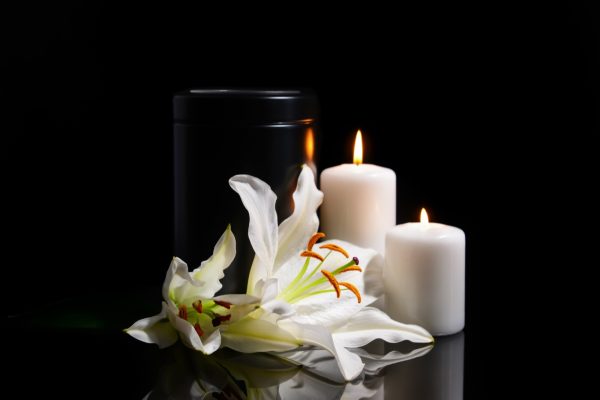 A mortuary urn beside burning candles and white lily flowers, representing families harmed by the mishandling of human remains in California.
