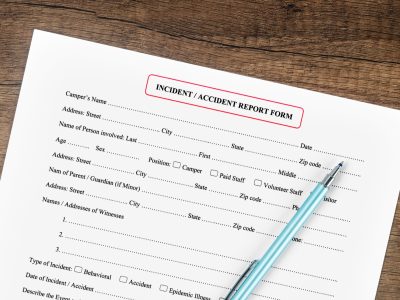 A blank accident report form and pen on a wooden desk, the incident report a business asks you to complete after a slip or trip and fall.